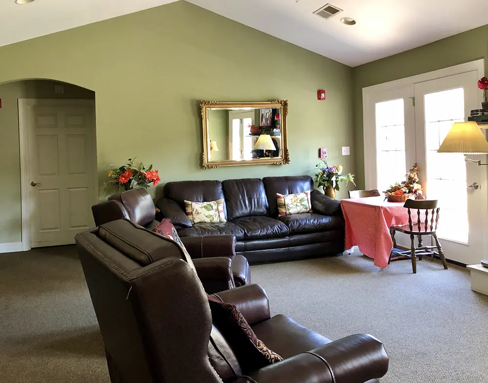 Warm and inviting living room at The Carriage House with leather furniture, green walls, and natural light