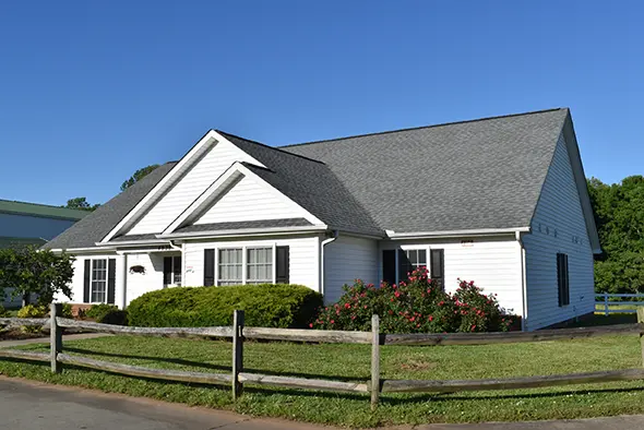 The Carriage House, a white single-story home with black shutters, gray roof, and landscaped garden.
