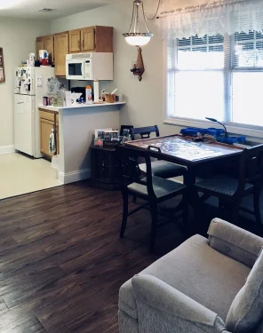 Private room at Lamoor Commons with small kitchen, wood cabinets, dining table, and large window