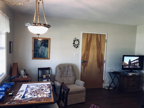 Lamoor Commons private room with armchair, puzzle table, framed art, and TV setup